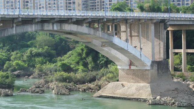 Concrete arch bridge spanning a green river with urban apartments in background in Yizhou, Guangxi China. Regional transport infrastructure, river crossing, and regional Chinese city development