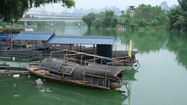 Weathered wooden fishing boats moored on a calm river with karst mountains in Guangxi China. Authentic rural riverine lifestyle. Traditional fishing, cultural heritage, and regional tourism 广西河池怀远