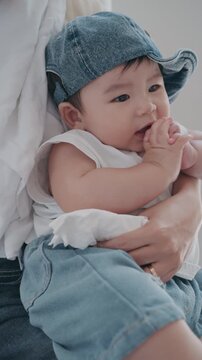 4K Vertical close up of a cute Asian baby boy wearing a denim hat in his mother's arms.