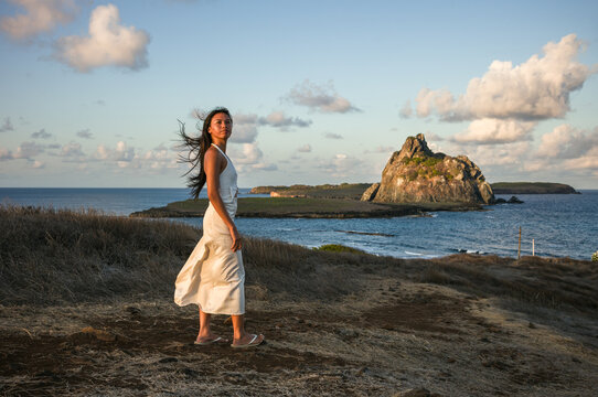 Asian woman in a dress at a clifftop viewpoint over the sea, Fernando de Noronha, Pernambuco, Brazil