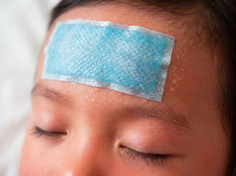 Close-up of a sick child with a fever, resting peacefully with a blue cooling gel patch on their forehead for temperature relief and comfort.