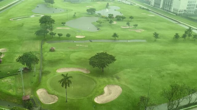 An aerial view of a golf course during heavy rain, with raindrops clearly visible passing in front of the camera.