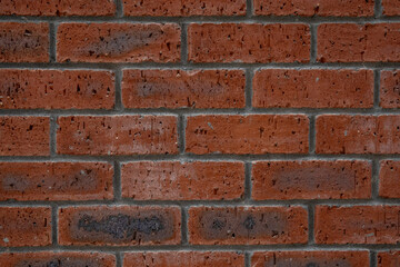 Fototapeta premium Weathered red brick wall texture with rich terracotta and crimson tones. A rigid masonry grid featuring a rough matte finish and dark charcoal accents for versatile industrial design utility.