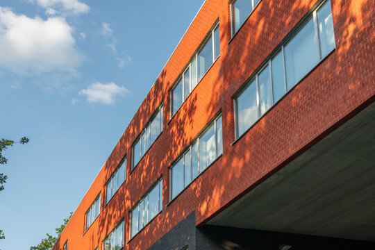 Contemporary university building with red brick facade, blue sky and tree shadows