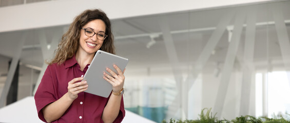 Fototapeta premium Smiling businesswoman browsing information, engaged in corporate or business communication via digital tablet in corporate office, copyspace banner. Technology, professional application use concept