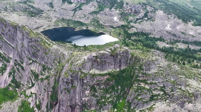  Breathtaking aerial view of a pristine mountain lake surrounded by sharp rocky peaks and dense green pine forest on a bright summer day.