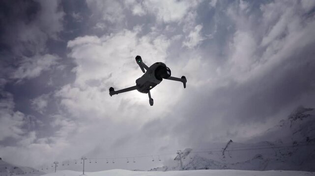 Quadcopter drone hovering with yaw rotation against a dramatic mountain sky above a snowy alpine landscape, highlighting multirotor flight stability and UAV technology, static upward view, Mendoza