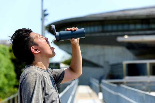 猛暑の夏に水筒でスポーツドリンクを飲み汗で失われた電解質とミネラルを補給しダイエットに臨む男性