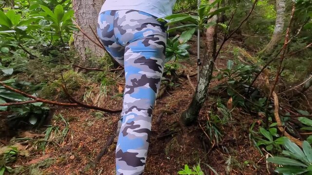 Female hiker walking rear view through dense Georgian forest, using trekking poles on narrow woodland trail for hiking route footage, outdoor endurance, eco tourism, forest navigation, and adventure