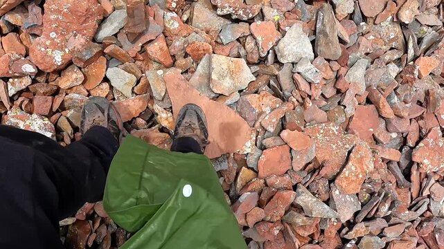 Hiker descending in close-up over loose mountain scree, stepping down rocky slope in rain jacket during trekking route for hiking safety, trail risk, outdoor tourism, and mountain travel content