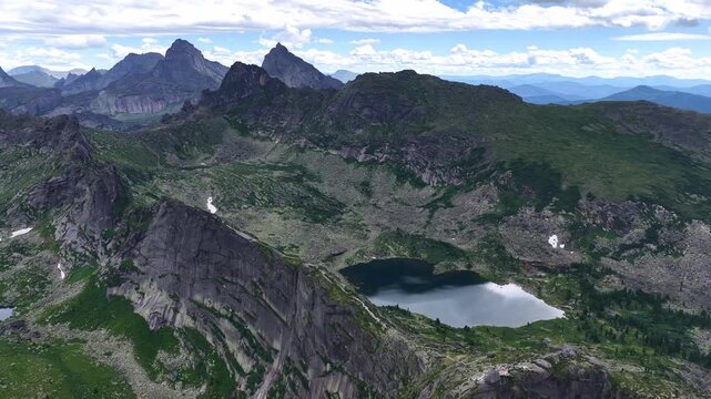  Breathtaking aerial view of a pristine mountain lake surrounded by sharp rocky peaks and dense green pine forest on a bright summer day.