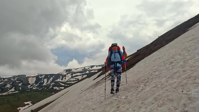 Female hiker crossing snow slope wide shot in Georgia, using trekking poles on alpine route with mountain ridges for hiking tourism, snow travel, route planning, and expedition training footage