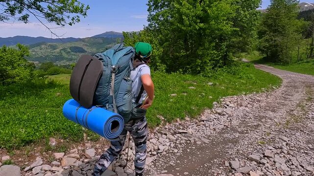 Woman hiking side view shot in rural Georgia, carrying camping gear on gravel mountain road for trekking tourism, outdoor expedition, travel planning, endurance training, and route content.