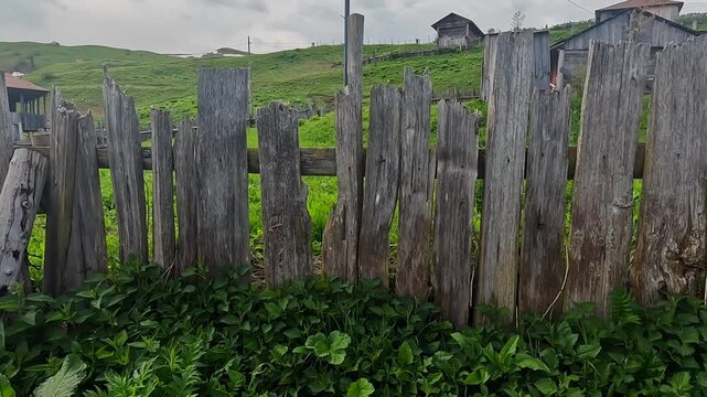 Camera passing wooden fence wide shot in rural Georgia, showing weathered boards, farm houses, green hills, and village landscape for agriculture, countryside travel, and regional heritage content