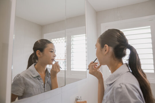 Teenage Girl Applying Lipstick in Bathroom Mirror