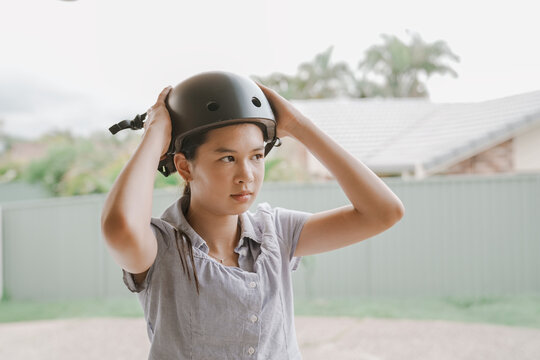 Teenage Girl Putting On Bike Helmet Outdoors