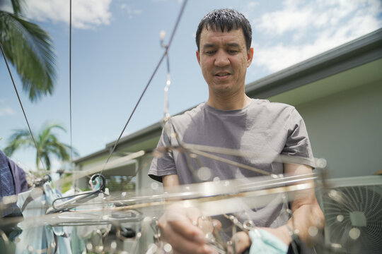 Laundry, drying clothes, man, household chores, domestic life, washing, lifestyle of a mid adult male hanging garments on a clothesline in a sunny backyard on a summer day.