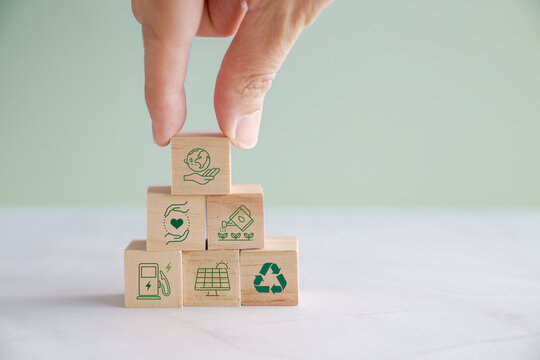 Hands holding wooden blocks with green sustainable environmental icons, renewable energy concept
