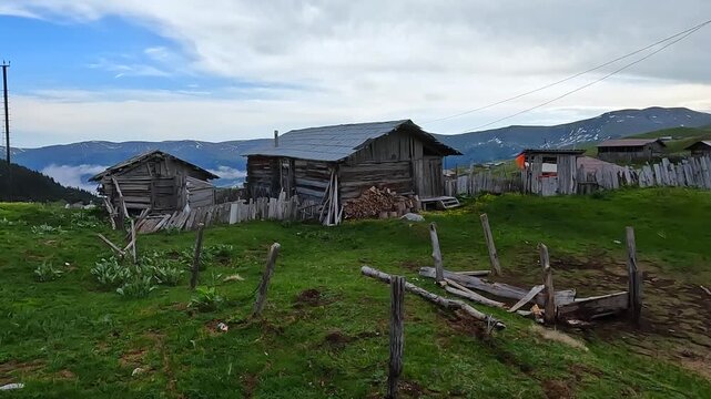 Georgian village panning in wide shot across wooden houses, fenced pasture, cloud layer, and mountain slopes for Caucasus travel, rural heritage, highland tourism, and regional documentary footage