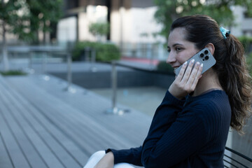 Fototapeta premium Side view of a young Latina businesswoman talking on a smartphone with copy space in a corporate campus.