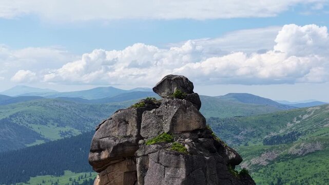 High-angle aerial drone view of a majestic mountain range with sharp rocky peaks, lush green pine forests, and pristine alpine lakes under a dramatic sky with scattered clouds