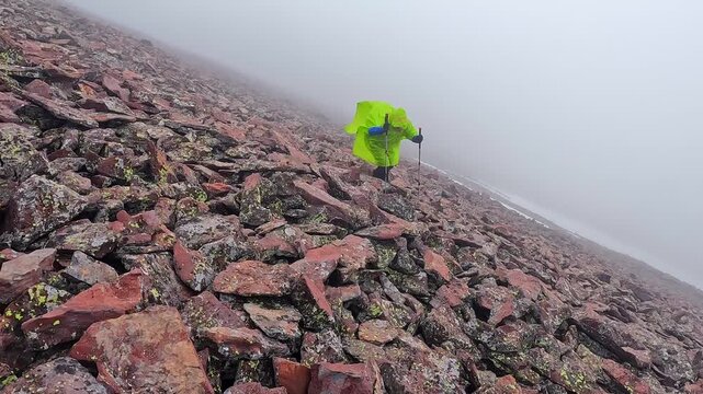 Hiker climbing in wide shot on Didi Abuli mountain, moving uphill across loose volcanic scree in strong wind and fog for Georgia trekking, alpine route difficulty, hiking safety, and adventure travel