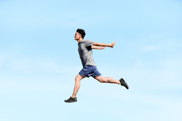 Obraz premium 青空を背景に空中で飛び跳ねる20代から30代の日本人の男性のアスリートの達成感を表現する横向きの全身