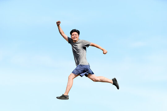 青空を背景にジャンプしてガッツポーズをし自由や開放感や目標達成を表現する健康的な30代から40代男性