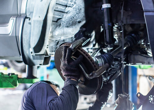 Professional mechanic replacing car brake disc and suspension components in a garage workshop.