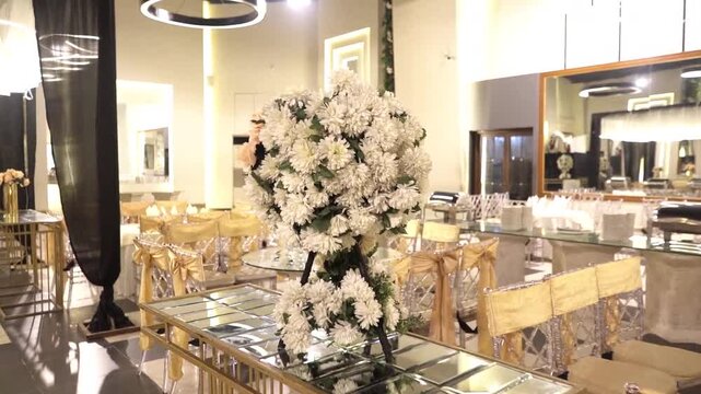 Elegant wedding reception setup featuring luxury banquet hall decor, floral centerpiece arrangements, transparent chairs, modern lighting, and sophisticated event styling.