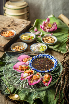 Delicious Miang Kham Bua Luan, a traditional Royal Thai appetizer featuring vibrant pink lotus petals, toasted coconut, fresh herbs, and sweet savory dipping sauce served on a wooden table.