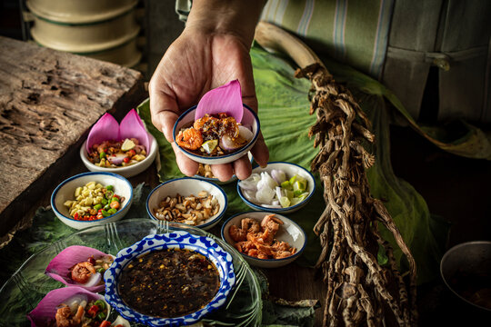 Delicious Miang Kham Bua Luan, a traditional Royal Thai appetizer featuring vibrant pink lotus petals, toasted coconut, fresh herbs, and sweet savory dipping sauce served on a wooden table.