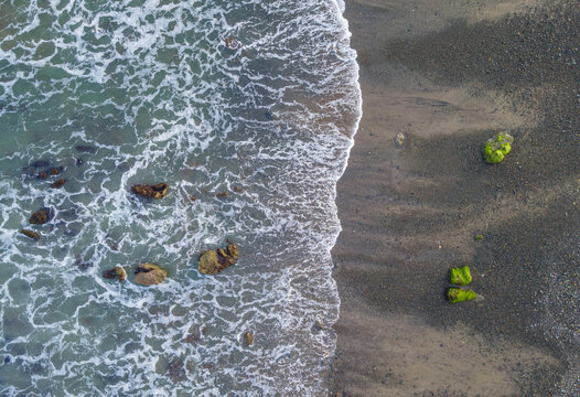 Aerial View of Scenic Watubale Beach with Mossy Rocks and Crashing Waves at Sunset, Drone view of a Beach featuring moss-covered coastal rocks and dramatic waves