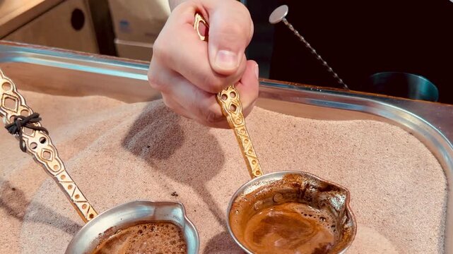 Traditional Turkish coffee brewing in copper cezve pots on hot sand close up. Authentic oriental method of making strong espresso with thick foam on street market. Middle eastern culture lifestyle.