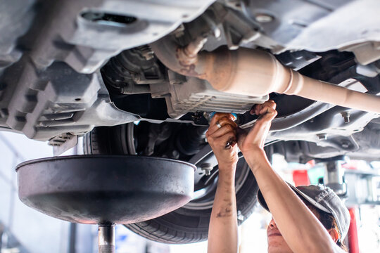 Car maintenance process: draining old engine oil at service station.