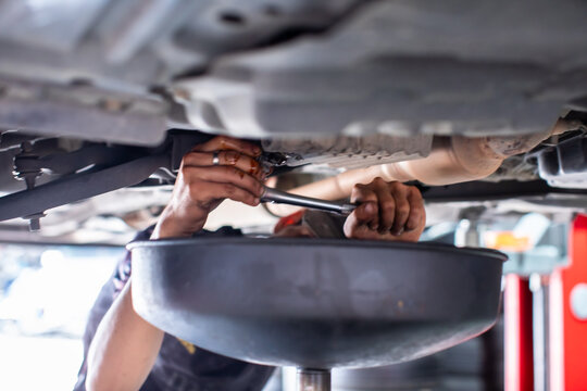 Car maintenance process: draining old engine oil at service station.