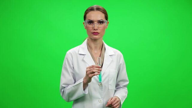 Female scientist in white lab coat examining test tube with blue liquid isolated on green screen