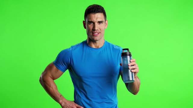 Fit athletic man in blue t-shirt holding a water bottle and smiling on a green screen