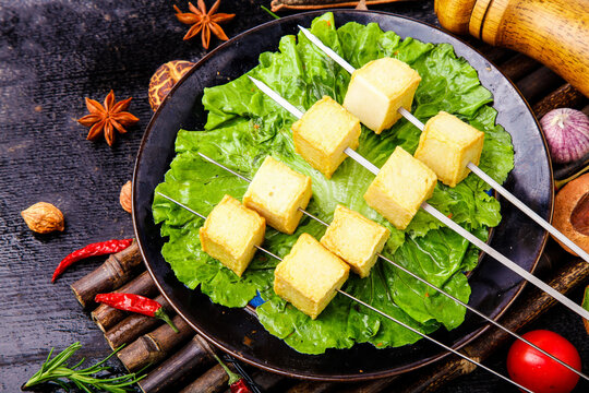 Grilled tofu skewers with fresh lettuce and Asian spices on rustic wooden table