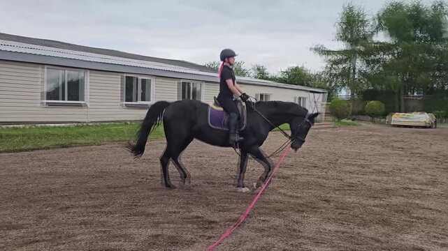 Rider practices skills on black horse in training area during cloudy day