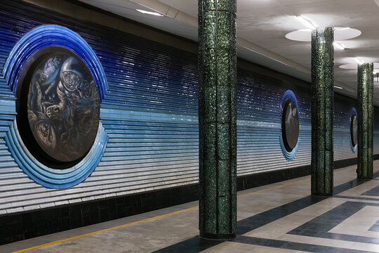 Kosmonavtlar metro station in Tashkent featuring green columns and ornate ceiling sculpture. Symmetrical underground hall with marble floors and commuters, ideal for travel and architecture.