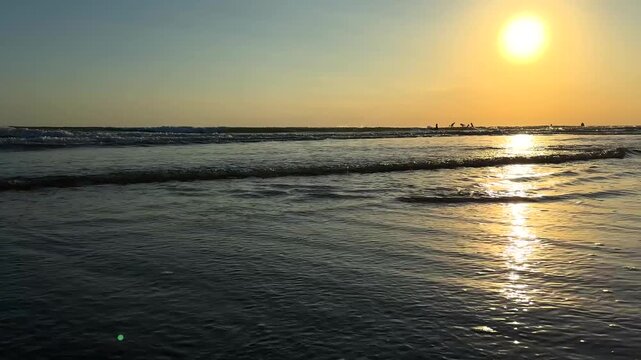 Golden sun sets over gentle ocean waves at beach, casting warm light on water. Summer relaxation and enjoyment concept. Soft sounds of waves enhance peaceful outdoor experience