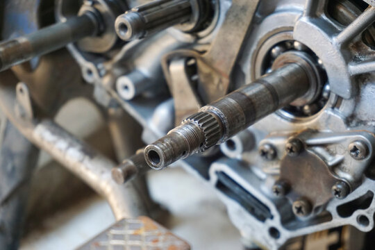 A detailed close-up shot of an open motorcycle engine crankcase during repair, showing the main transmission shaft, ball bearings, splines, and metallic casing assembly in a garage.