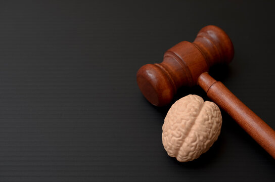 Wooden Judge Gavel next to Human Brain Model on Black Background for Mental Health Law Concept