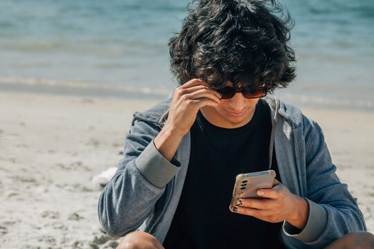 Vacation and technology. Portrait of young  man using smartphone on the beach