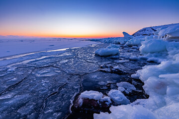 Beautiful winter landscape featuring broken ice floes, pancake ice, and snow accumulation along a freezing Nordic shoreline at sunset, captured during the golden hour in Finland. © Artem