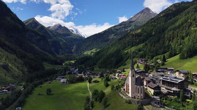 Hof, Austria - June 11 2026: Aerial drone footage of Pfarrkirche Heiligenblut, church in Hof, Austria. Beautiful weather with snowy mountains in the background. Heaven in the Austrian Alps. Grossglock