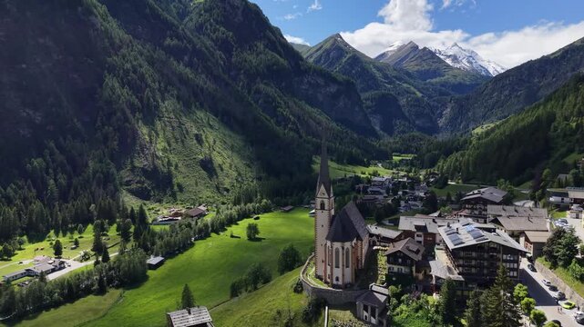 Hof, Austria - June 11 2026: Aerial drone footage of Pfarrkirche Heiligenblut, church in Hof, Austria. Beautiful weather with snowy mountains in the background. Heaven in the Austrian Alps. Grossglock