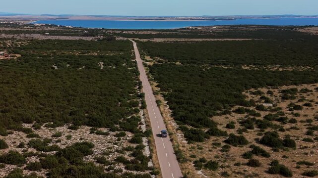 Silver camper van car driving on a road toward the blue Adriatic Sea, Pag Island, Croatia. Aerial