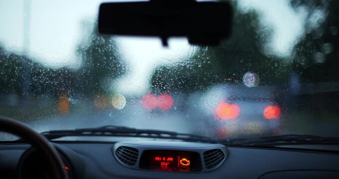 Point of view drive in city on a rainy day with water drops on windshield and blur vehicle ahead showing left turn signal